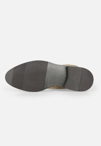 Suela de zapato de ante marrón con forma redondeada, que presenta una suela exterior de goma negra texturizada y un inserto de cuero beige liso.