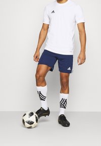 White short-sleeved shirt, navy shorts, black soccer cleats, black and white patterned socks, and a black-and-white soccer ball.