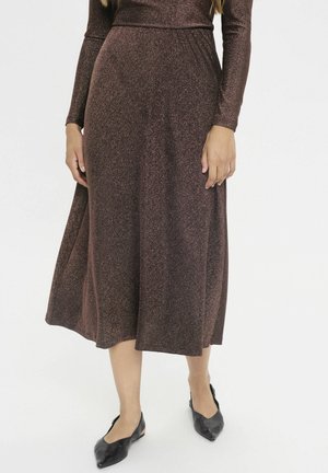 Langes bronzefarbenes Kleid mit langen Ärmeln, tailliertem Schnitt und einem fließenden Rock. Der Stoff hat einen subtilen Schimmer und eine glatte Textur. Schwarze Ballerinas.