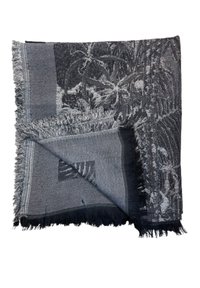 Couverture tissée dans des nuances de gris avec un bord texturé et à franges. Présente un motif de feuille de palmier et un design géométrique sur différentes sections.