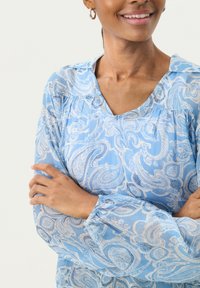Blusa azzurra chiara con motivo paisley e dettagli bianchi, scollatura a V e maniche arricciate. Tessuto morbido e leggero.