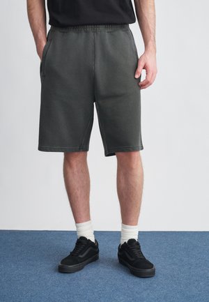 Sötétszürke, puha anyagból készült rövidnadrág, rugalmas derékpánttal, oldalzsebekkel és kényelmes szabással, fekete tornacipővel és fehér zoknival párosítva.