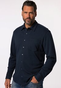 Camisa de botones de manga larga en color navy, hecha de tela texturizada, con un bolsillo en el pecho y botones plateados, combinada con jeans azules informales.