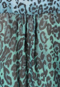 Un pannello di tessuto presenta un design a macchie di leopardo in turchese e nero con una sottile texture. La parte superiore è arricciata, creando pieghe al centro.
