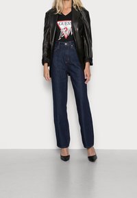 Černá kožená bunda, grafické černé tričko s červeným a bílým logem, džíny s vysokým pasem v modré barvě a černé špičaté baleríny.