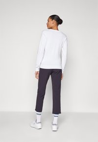 Suéter branco de mangas longas com um corte ajustado, combinado com calças curtas escuras e sapatos brancos. As meias têm riscas azuis e brancas.