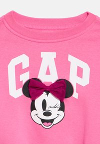 Rozā kokvilnas džemperis ar baltu "GAP" uzrakstu, tam pievienots Minnijas Peles attēls un violets auduma loks. Apaļa kakla izgriezums.