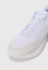 Baskets de sport blanches avec des motifs en relief, lacets blancs et un logo swoosh visible sur le côté et la zone des orteils.