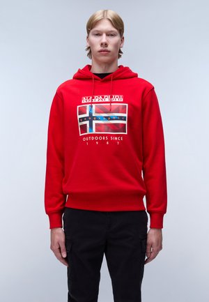 Rode hoodie met een grafische print met een vlagontwerp. Geribbelde manchetten en zoom. Model gecombineerd met zwarte broek. Eenvoudige achtergrond.