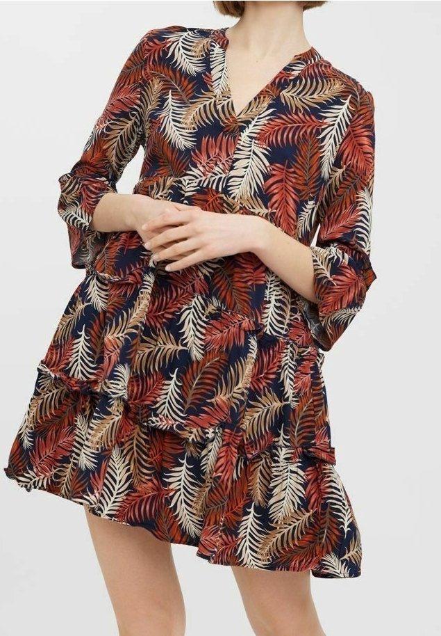 Femme portant une robe mini à manches longues, col en V, à volants, avec un fond bleu marine et un motif de feuilles rouges, orange et crème.
