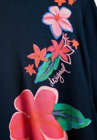 Mustaa ribbineulosta, jossa on suuret, värikkäät kukkakuviot vaaleanpunaisina, oransseina ja vihreinä, "desigual"-teksti osana kuosia.