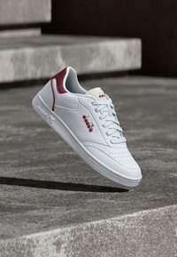 Λευκό sneaker από δέρμα με διάτρητη μύτη, ανοιχτομπλε κορδόνια και κόκκινες λεπτομέρειες στη φτέρνα και το λογότυπο. Υφή στη σόλα από καουτσούκ.