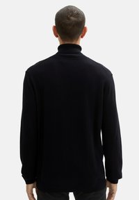 Pull en maille côtelée bleu marine avec col montant, manches longues et coupe décontractée. Texture douce et design minimaliste.