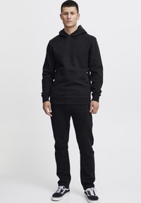 Sudadera negra con capucha y bolsillo tipo canguro, combinada con pantalones negros ajustados y zapatillas en blanco y negro. Textura suave, fit casual.