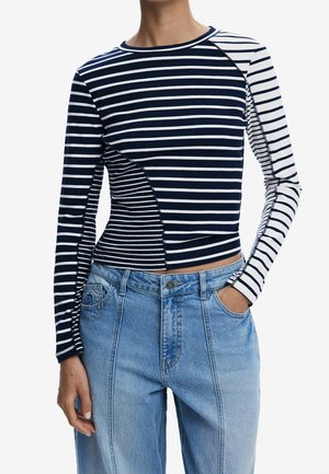 Haut à manches longues rayé avec des rayures horizontales mêlées bleu marine et blanc, associé à un jean taille haute bleu clair. Une main dans la poche.