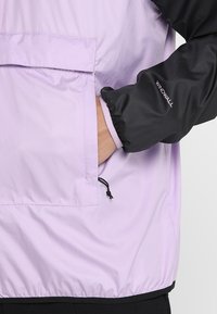 Windbreaker in lichtlavendel met zwarte mouwen. Beschikt over een voorkantzak en een verstelbare zoom met trekkoord. Glad, lichtgewicht materiaal.