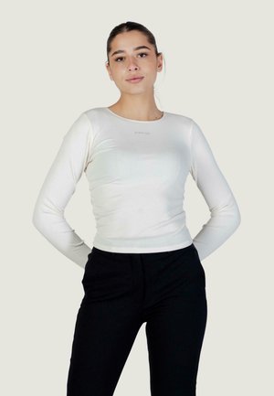 Top bianco a maniche lunghe con trama a coste e scollo rotondo; presenta un marchio discreto sul petto; abbinato a pantaloni neri.