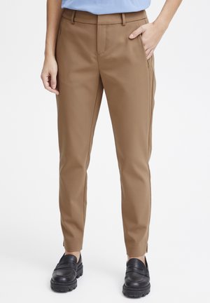 Ušité hnědé kalhoty z hladké tkaniny, s bočními kapsami, slim fit a tapered nohavicemi, obuté s černými nazouvacími botami.