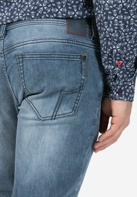 Vervaagde blauwe denim jeans met een rechte snit, voorzien van achterzakken, subtiele stiksels en een merklabel met rode accenten op de tailleband.