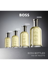 Vier BOSS Bottled Eau de Toilette-flessen in oplopende maten: 30ml, 50ml, 100ml en 200ml, geëtaleerd op een grijs oppervlak.