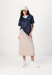 Marinblå kortärmad polo med teal-färgad krage, beige midi-kjol och vita sneakers. Inkluderar varumärkeslogotyp på skjortan och elastisk midja på kjolen.
