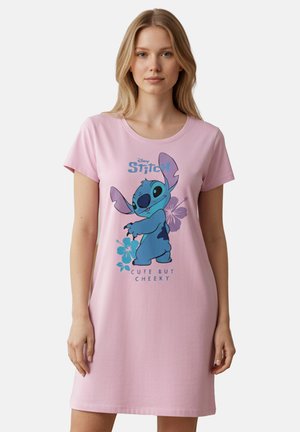 Giovane donna che indossa un abito rosa con il personaggio blu Stitch e la scritta "Carina ma impertinente" sul davanti.