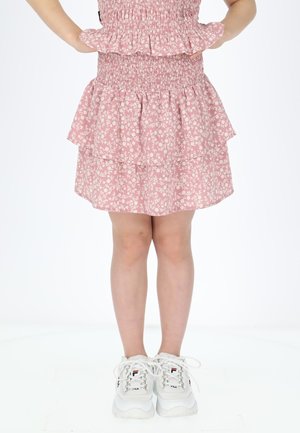 Roze jurk met bloemenpatroon, een smocked lijfje en gelaagde ruffles. Een paar witte sneakers met rode en zwarte accenten.
