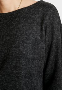 Pull en gris charbon fabriqué à partir d'un tissu à mailles texturé, doté d'un large col et d'épaules légèrement tombantes pour une coupe décontractée.