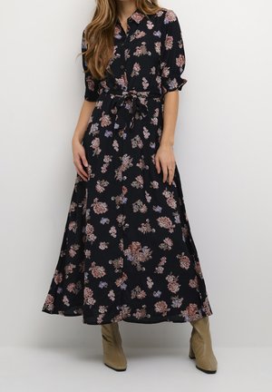 Robe maxi florale en tissu noir avec des motifs de fleurs colorées, fermeture à boutons sur le devant, manches courtes et détail de taille nouée. Présentée avec des bottes à talons beiges.