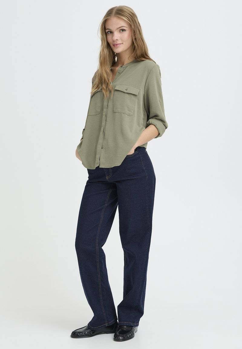 Olivgrünes Hemd mit Knöpfen, zwei Brusttaschen, kombiniert mit dunkelblauen Straight-Leg-Jeans und schwarzen Slippern. Glattes Material, lässige Passform.