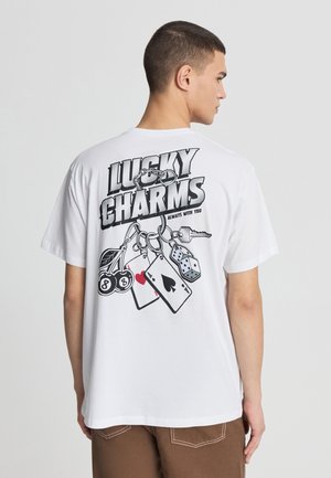 Biała bawełniana koszulka z nadrukiem na plecach, zawierająca tekst "LUCKY CHARMS" oraz ilustracje kart, wiśni i kostki do gry.