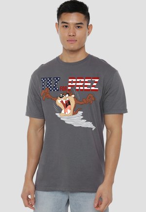 Young man wearing gray T-shirt with cartoon character Taz spinning in a tornado and text "Taz for Prez" in American flag pattern.