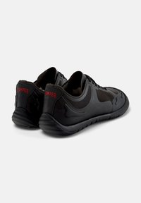Black athletic shoes featuring a mesh upper, rubber sole, and embossed design, with "GAMPER" logo in red on the heel.