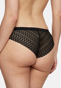 Czarne koronkowe figi z falbanką, z geometrycznym wzorem, przezroczystą teksturą i jednolitą czarną gumką w talii.