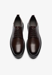 Brown leather shoes with a polished finish, featuring a classic lace-up design, round toe, and black rubber sole. Minimalist style.