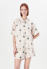 Chemise beige clair à manches courtes et short assorti, présentant des motifs de palmiers noirs, une fermeture à bouton et une coupe décontractée. Texture lisse.