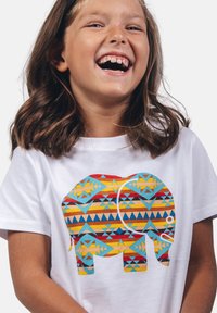Camiseta blanca con un gráfico de elefante colorido y patrones geométricos en azul, rojo, amarillo y naranja. Mangas cortas, corte casual.
