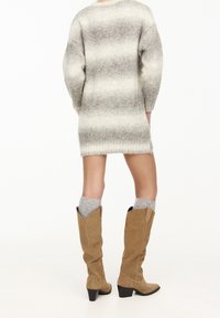 Robe en tricot de couleur gris clair avec des rayures gris foncé, offrant une coupe décontractée et des poignets côtelés ; associée à des bottes en daim marron clair et des chaussettes grises.