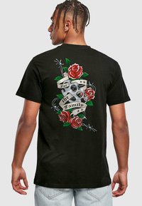 Black t-shirt featuring a graphic design of red roses, a skull, and a ribbon with the text "For the Family" on the back. Casual fit, short sleeves.