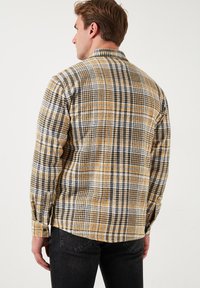 Langarm geruit shirt in tinten van geel, zwart en wit. Heeft een klassieke kraag en een losse pasvorm met zijsplitten.