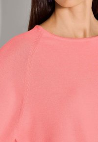 Lichtroze sweater met een brede halslijn, een losse pasvorm en een fijn gebreide textuur met zichtbare stiksels langs de naden.