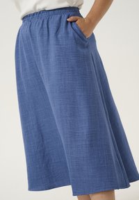 Culottes larges bleues avec taille élastique et poches latérales, dotées d'un tissu texturé et d'une finition lisse.