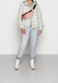 Chaqueta de plumas verde claro, suéter de punto gris, vaqueros azul claro y zapatillas altas blancas. Riñonera rosa con correa negra y cremallera.