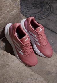 Paire de baskets de sport roses avec des semelles blanches et des rayures, posées sur des marches en pierre près d'une plaque d'égout en métal.