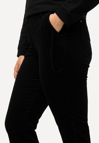 Zwarte corduroy broek met een slank ontwerp, zijzakken en een gestructureerde stof, met subtiele stikdetails langs de naden.