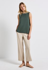 Top verde senza maniche con scollatura arricciata, abbinato a pantaloni beige a gamba larga e sandali con cinturini color cammello. Tessuto morbido e vestibilità comoda.