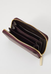 Calvin Klein wallet, burgundy with textured exterior, gold zipper, and three interior compartments lined in dark fabric.
