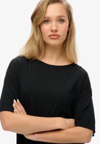 Camiseta negra de manga corta en una tela suave y ligera con un corte relajado y escote amplio, que presenta una textura suave y sin patrones visibles.