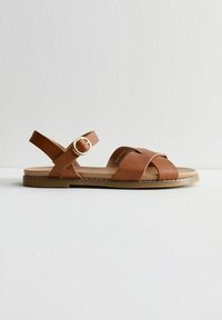 Bruna lädersandaler med korsade remmar, en justerbar vristrem med en cirkulär spänne och en platt gummisula.