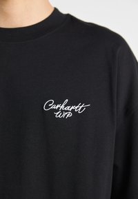 Crna dukserica od pamuka s okruglim izrezom. Ima bijeli izvezeni "Carhartt WIP" logo na lijevoj strani prsnog područja.